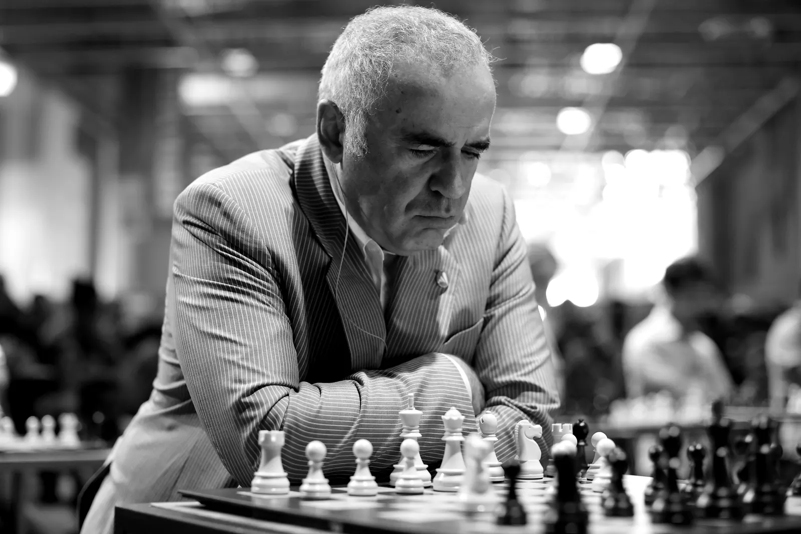Garry Kasparov leans over a chessboard, arms folded, studying the position.